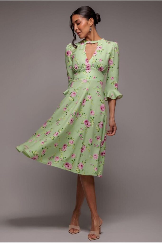 A woman wearing a floral print midi dress standing in a lush green garden setting, perfect for an outdoor wedding.